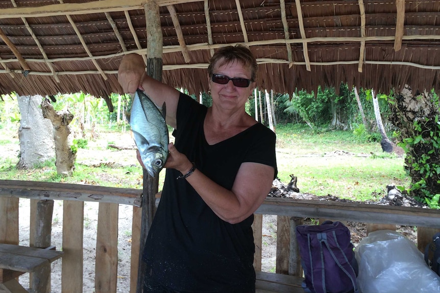 Joy Price holding a fish standing under a hut.