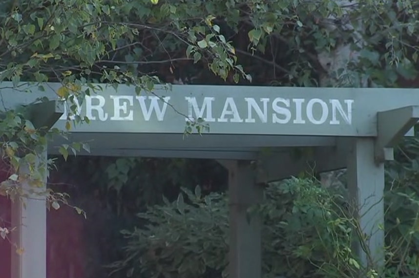 The front of an apartment building that says Drew Mansion with trees surrounding the entrance.