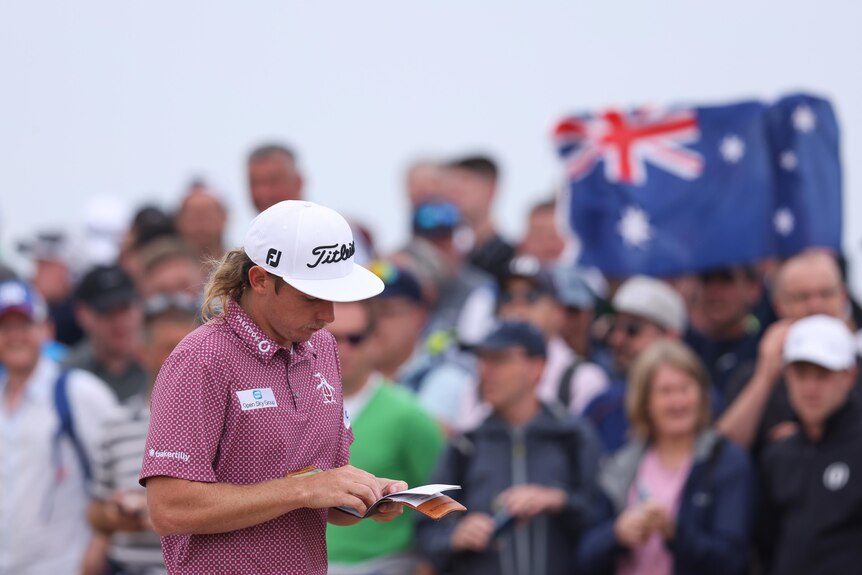 Cameron Smith looks at his yardage book, while an Australian flag is held up in the crowd behind him