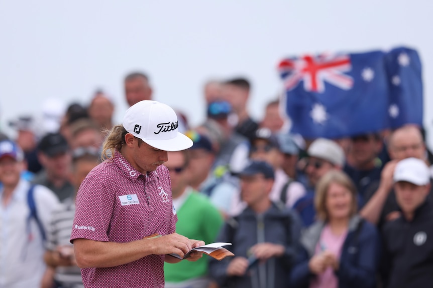 Cameron Smith mira su libro de yardas, mientras la multitud detrás de él sostiene una bandera australiana