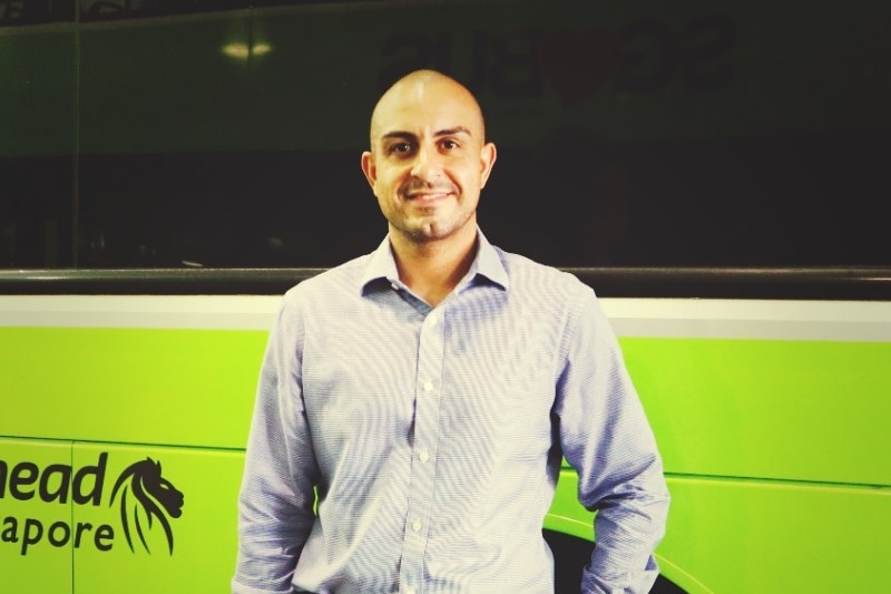 a man with a bald head and in business shirt stands in front of a green bus