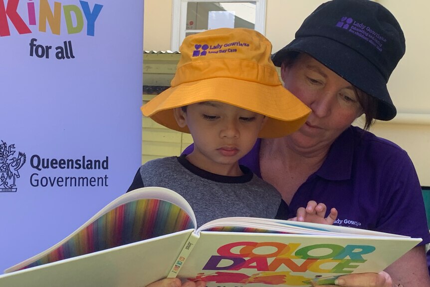 An educator with a child reading a book at a Queensland kindy.