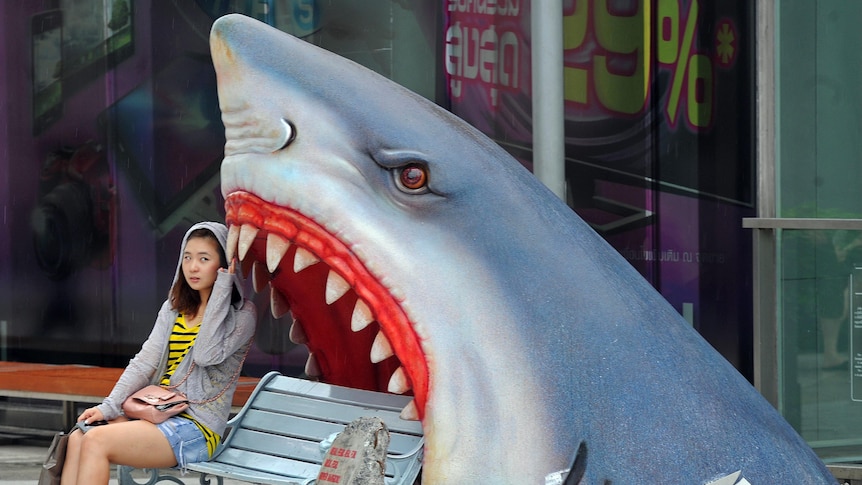 A woman sits next to a large art work of a shark at a shopping mall in Bangkok, Thailand.