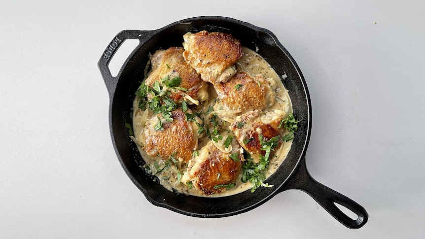 Browned chicken thighs in mustard-creamy sauce in cast iron pan with parsley garnish.