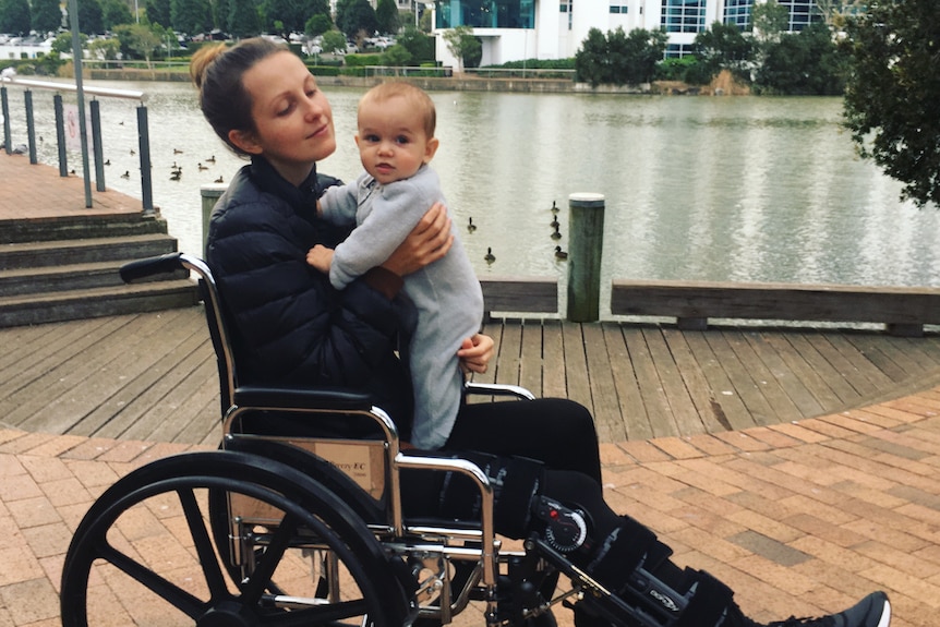 A young woman in a wheelchair holding her baby.