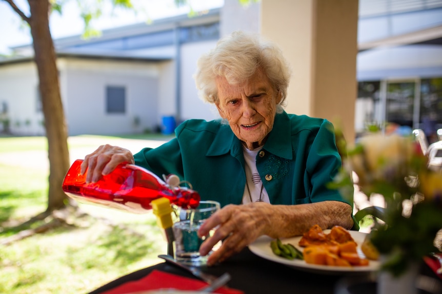 A young and an elderly woman eat food at a dining table outside on a sunny day.