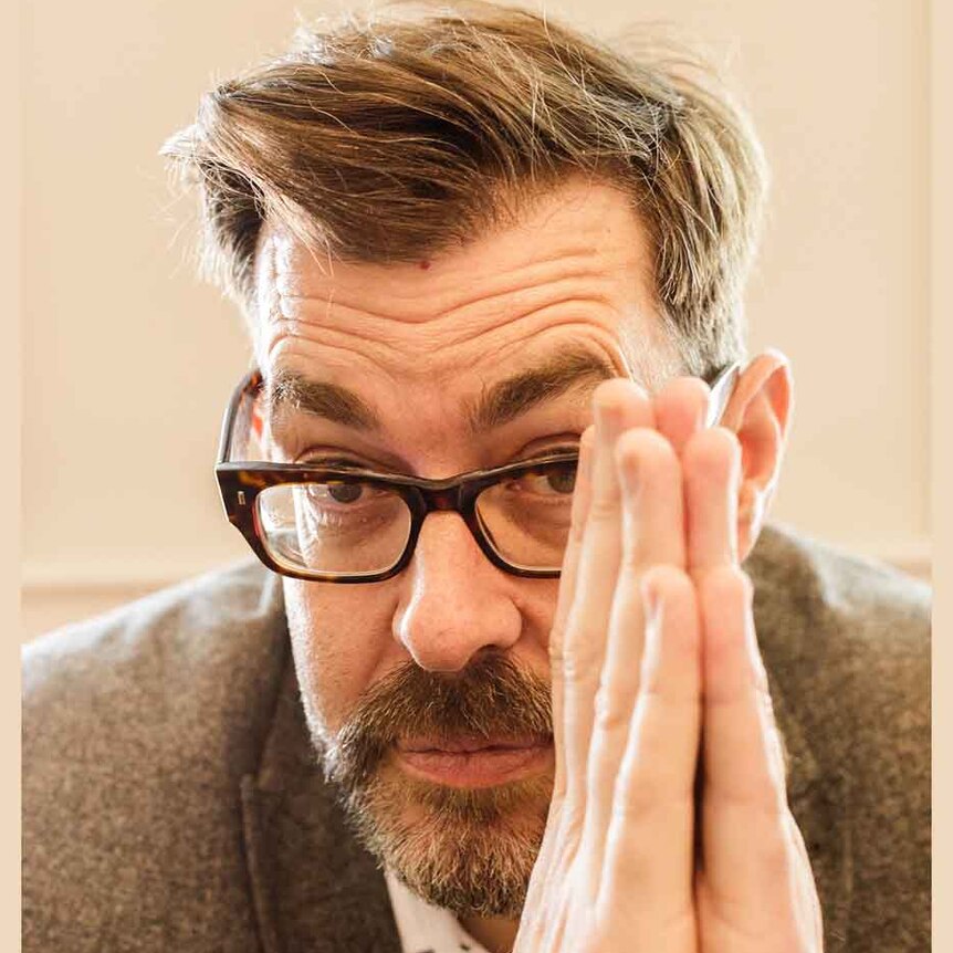 A tight crop of a man with glasses and hands together near his face