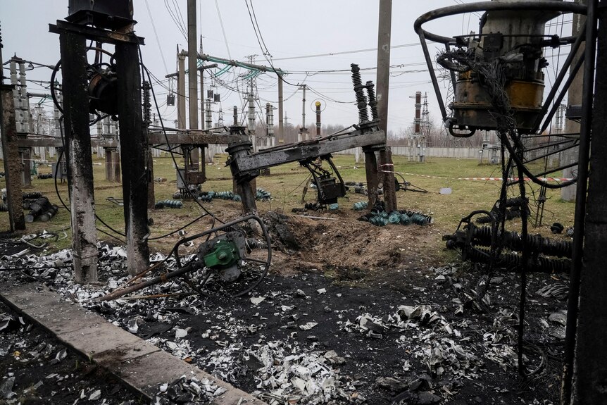 A heavily damaged, burnt and blackened electricity substation with wires and hardware lying on the ground.