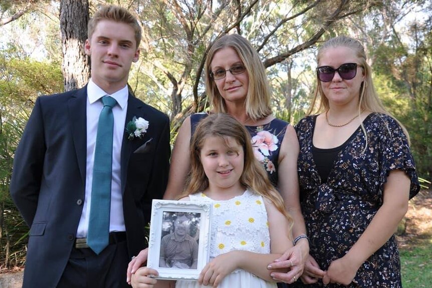 Three children and their mum holding a photo of their late dad.