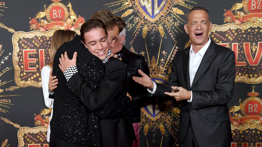 Tom Hanks smiles as his co-stars hug