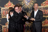 Tom Hanks smiles as his co-stars hug