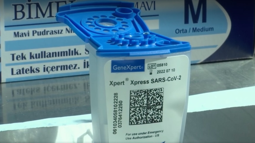 A single testing cartridge with a blue open lid and QR code sticker on the front.