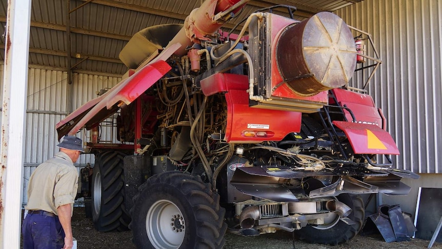 Farmer Ray Harrington standing beside a large red harvester with the seed destructor fitted to the back.