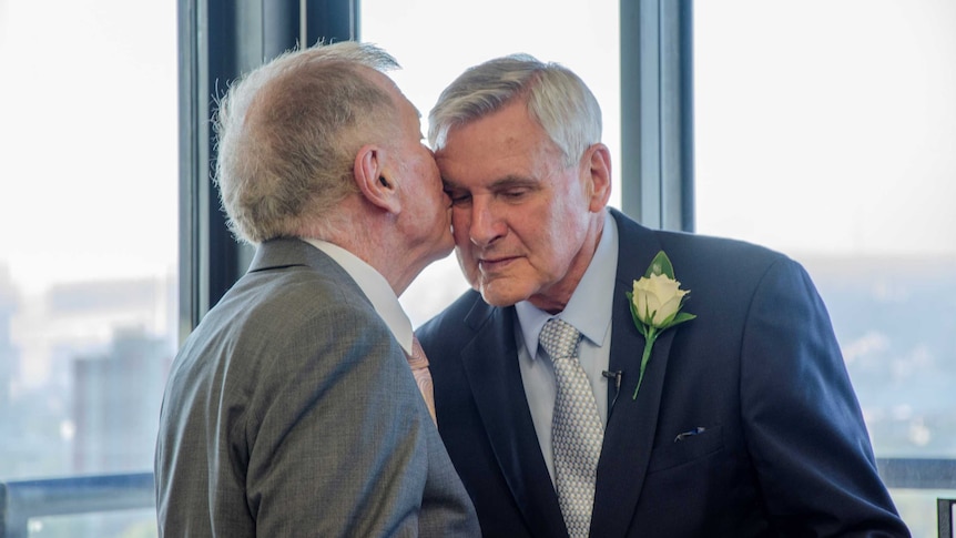 Two men hold hands and show their rings