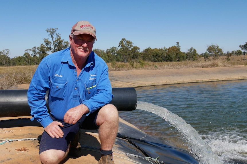 A man kneels on one knee on the edge of a dam with a water pipe gushing into it.