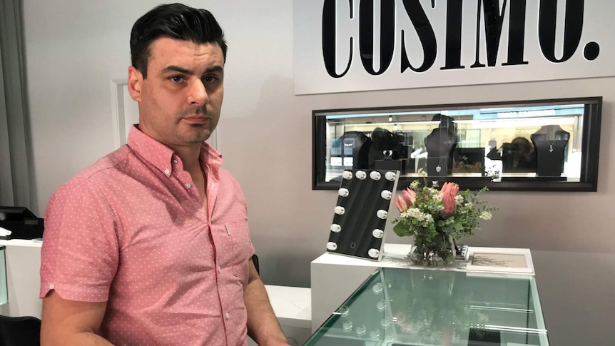 A man wearing a pink shirt looks at government pamphlets in his jewellery shop.