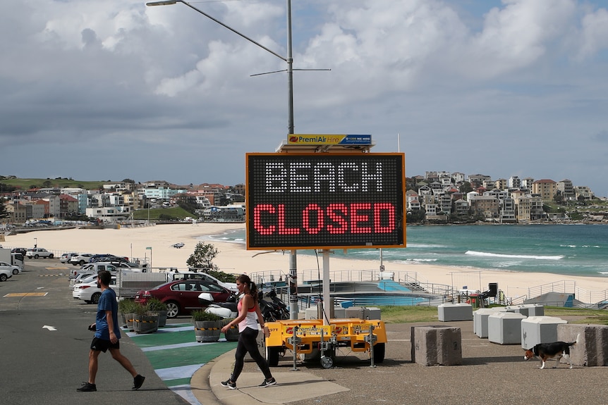 People walk past a "Beach Closed" sign at Bondi Beach