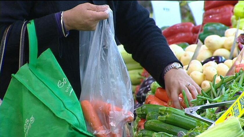 Shopper puts fresh produce into a plastic bag, while a reusable shopping bag hangs from their arm, June 2009