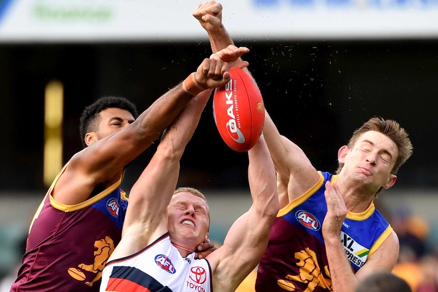 A Crows player unsuccessfully attempts to mark as two Lions players punch the ball away