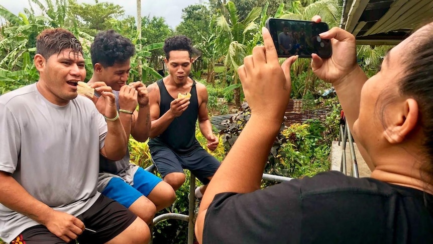 A woman takes a photo of three male athletes taking a food break