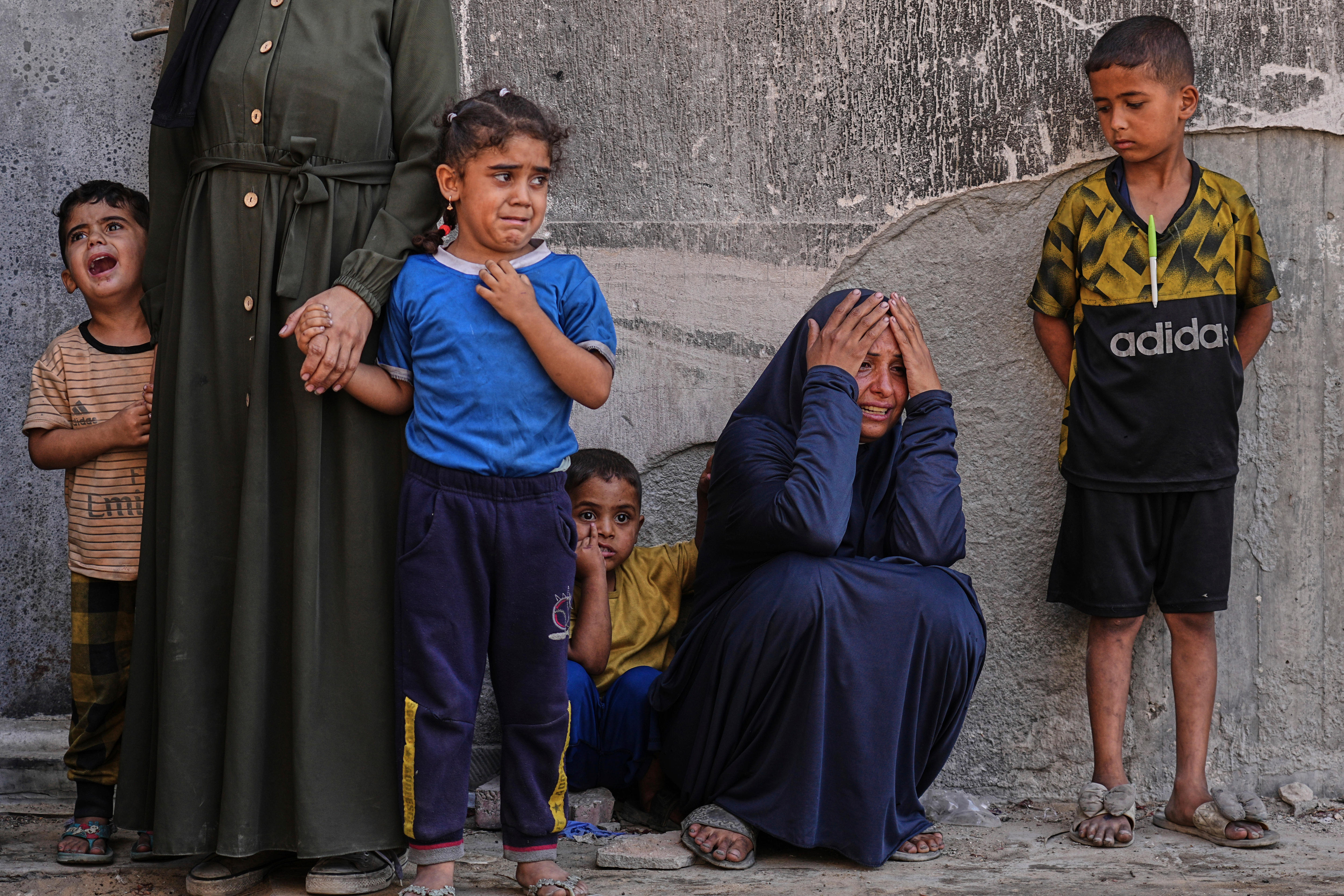Three children crying and a woman on her knees with her hands to her face looking distressed. 