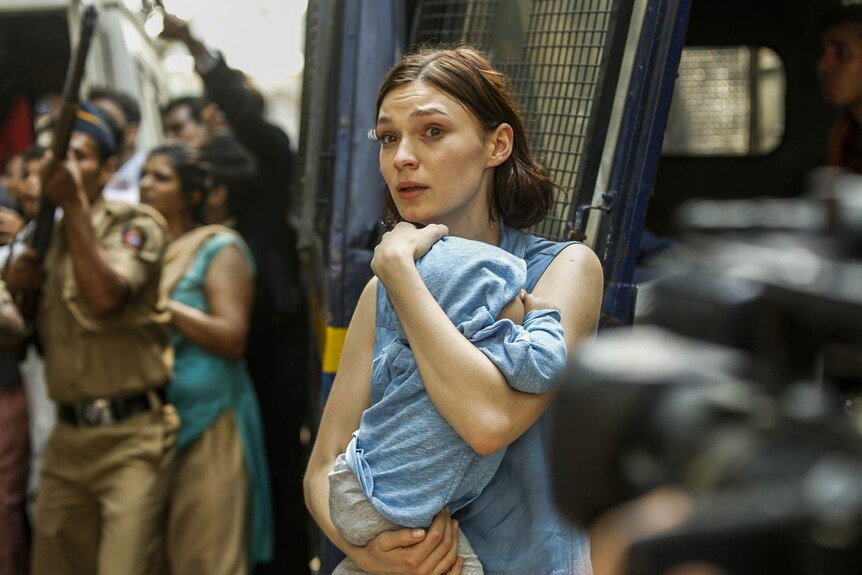 The actor, looking harrowed, holds an infant in a blue jumper to her chest.