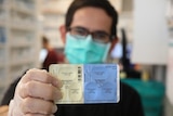A man wearing a surgical mask holding up a packet of antiviral drugs