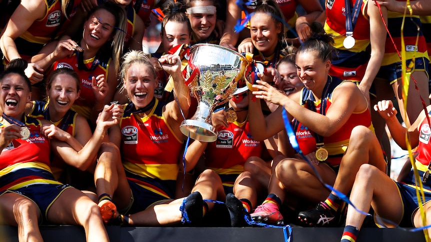 Erin Phillips and her Adelaide Crows teammates huddle around the premiership cup