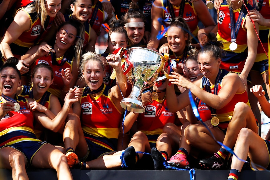 Erin Phillips and her Adelaide Crows teammates huddle around the premiership cup