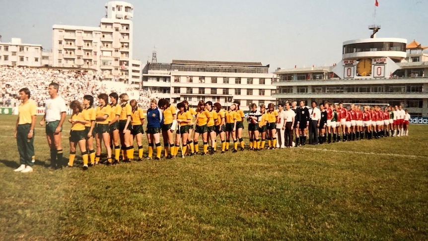 Two soccer teams, one wearing yellow and green and the other wearing red and white, line up before a game