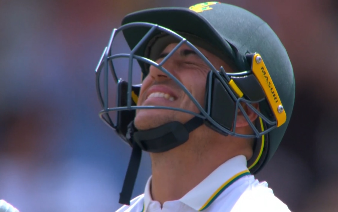 A close up shot of a cricket batter with green helmet throwing back head and grimacing