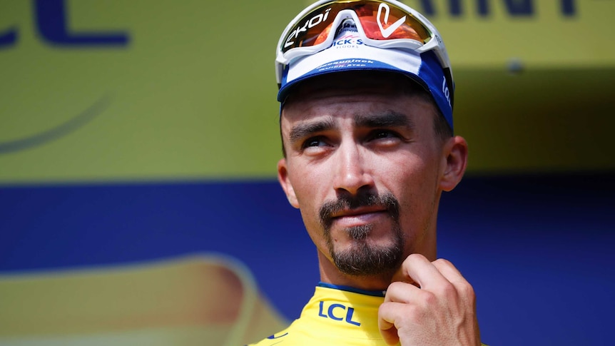 Julian Alaphilippe looks into the distance as he stands on the podium, holding a yellow jersey