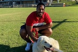 A rugby league player poses for a photo with a dog on an oval.