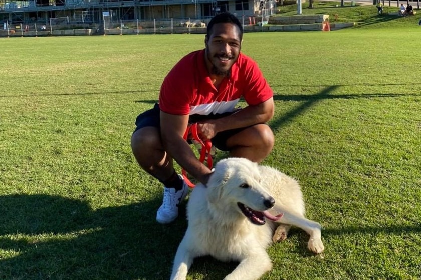 A rugby league player poses for a photo with a dog on an oval.