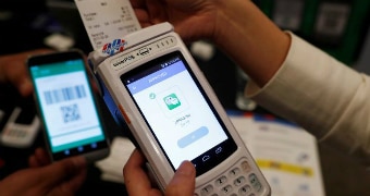 A worker guides a receipt out of a WizarPOS machine, which is lit up with an approved payment screen.