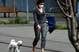 A woman wearing a mask and holding an umbrella walks with her dog.