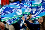 A group of people sit holding blue flags with 'Blues' written on them