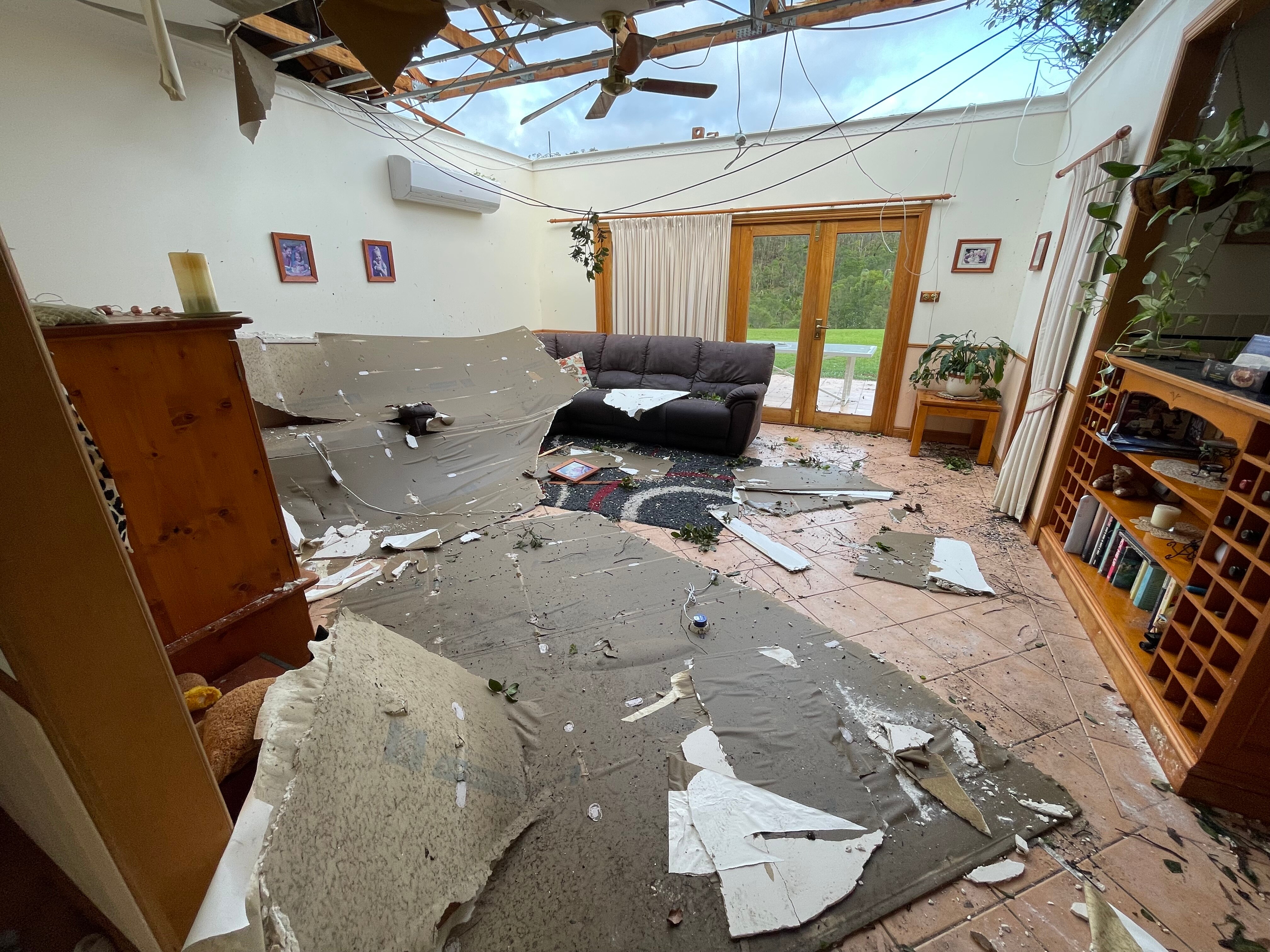 Roofing material and debris lays on a living room floor with a gaping hole in the roof. 