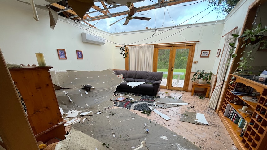 Roofing material and debris lays on a living room floor with a gaping hole in the roof. 