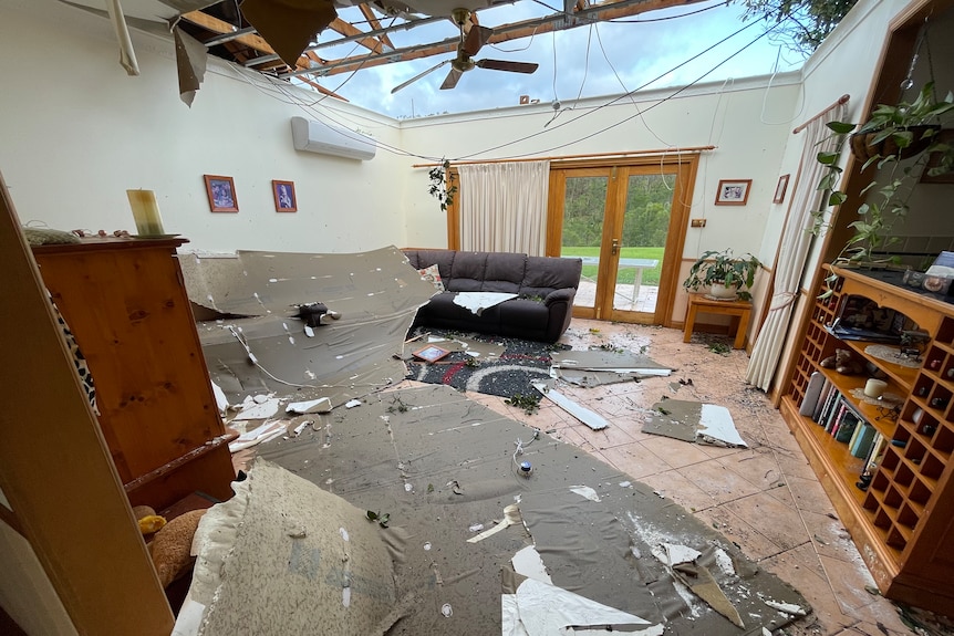 Roofing material and debris lays on a living room floor with a gaping hole in the roof. 
