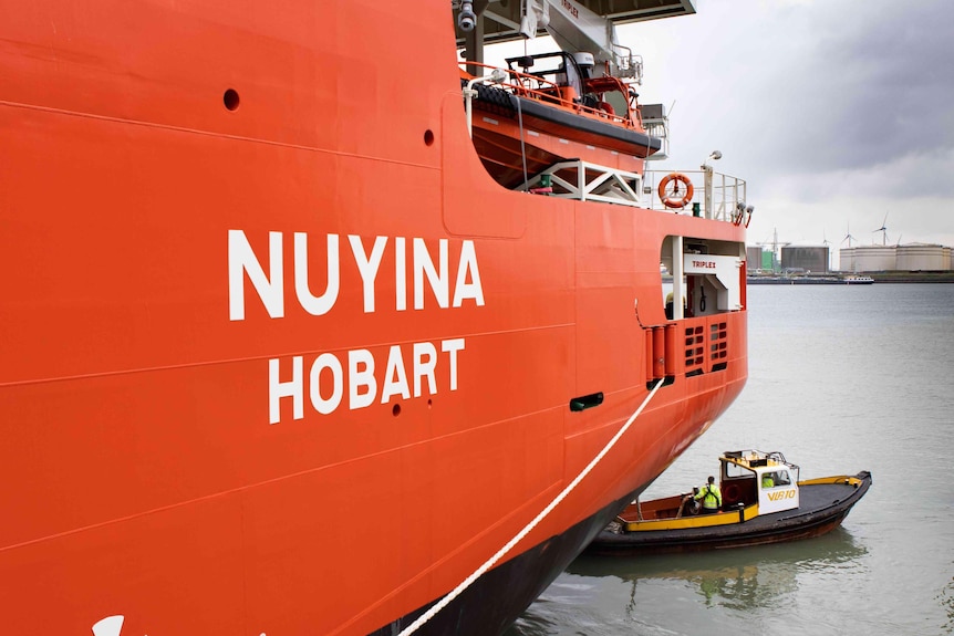 A large orange ship with name Nuyina Hobart and small black tug boat.