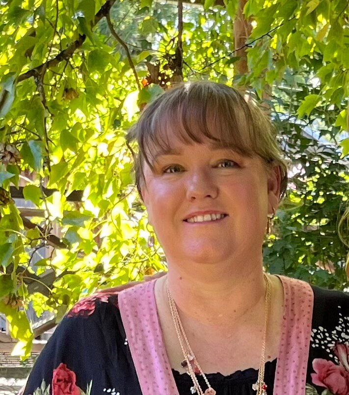 A close up of Kim Horn standing in front of a bush.