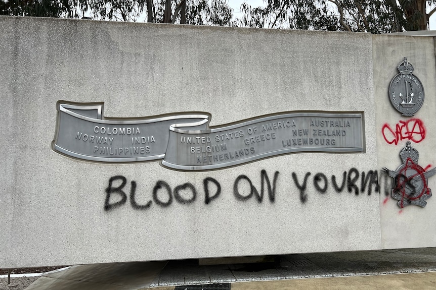 Black writing saying "blood on your hands" on a concrete memorial.