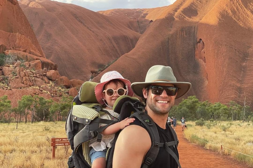 Baby girl in backpack with muscular man wearing wide brimmed hat with dark glasses