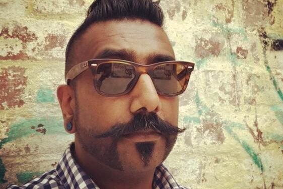 Samuel Jeyaseelan wearing sunglasses and taking a selfie in front of a brick wall.