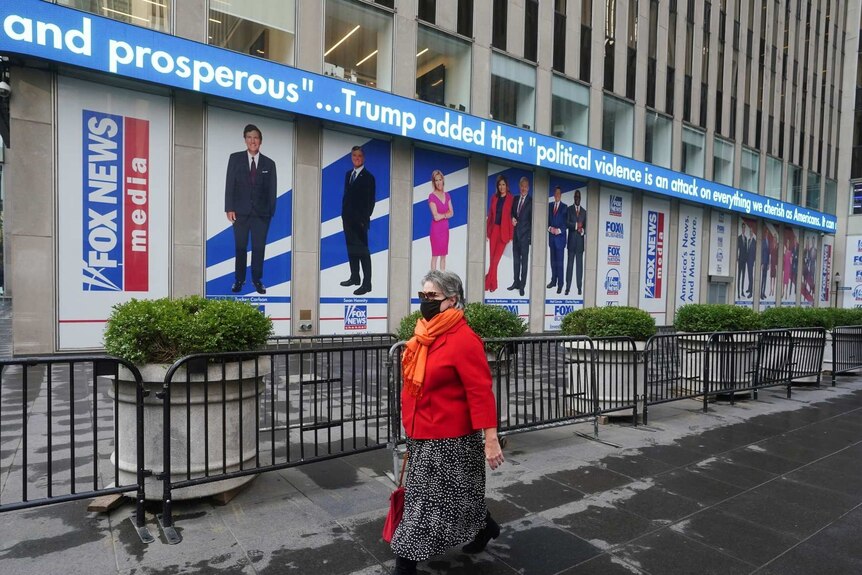 A woman walks outside Fox News Headquarters in New York City with pictures of hosts on the wall