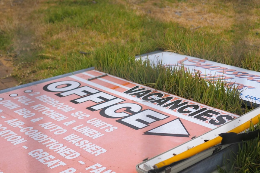 A damaged accommodation provider sign laying on the ground. 