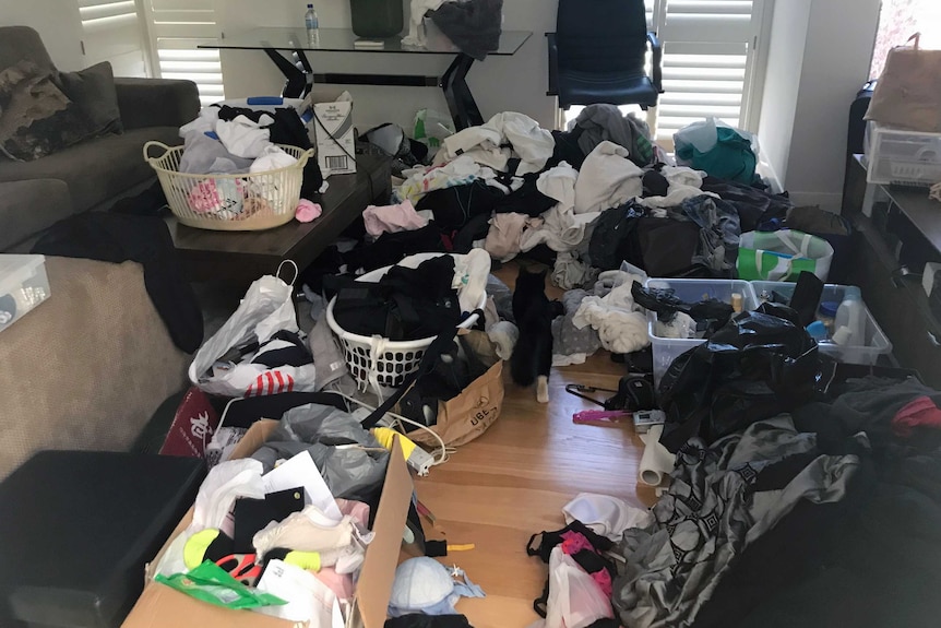 A lounge room filled with clothes and overflowing plastic containers and laundry baskets.