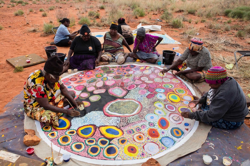 A group of Aboriginal artists working on a large painting.