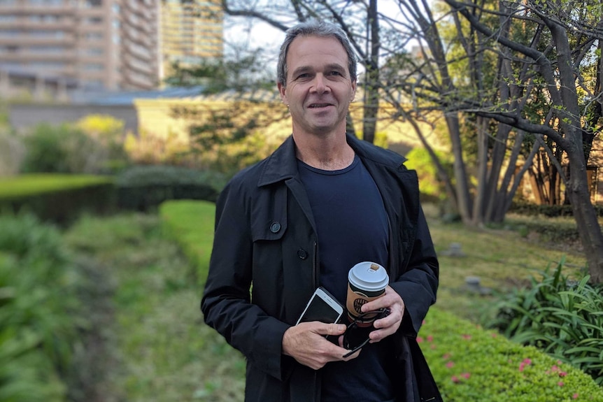 Paul Morgan stands in a coat with a coffee